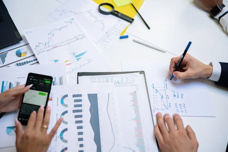 A modern workspace showing hands analyzing marketing data on a laptop and paper documents.